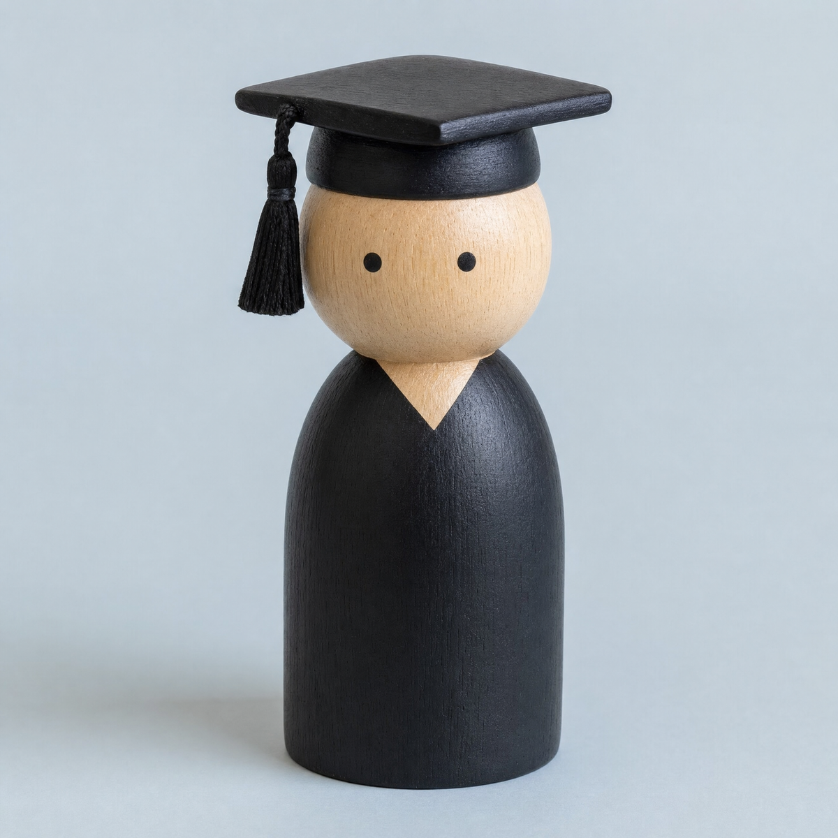 Jorlaxis Graduate: a wooden peg figure in a painted gown and mortarboard cap